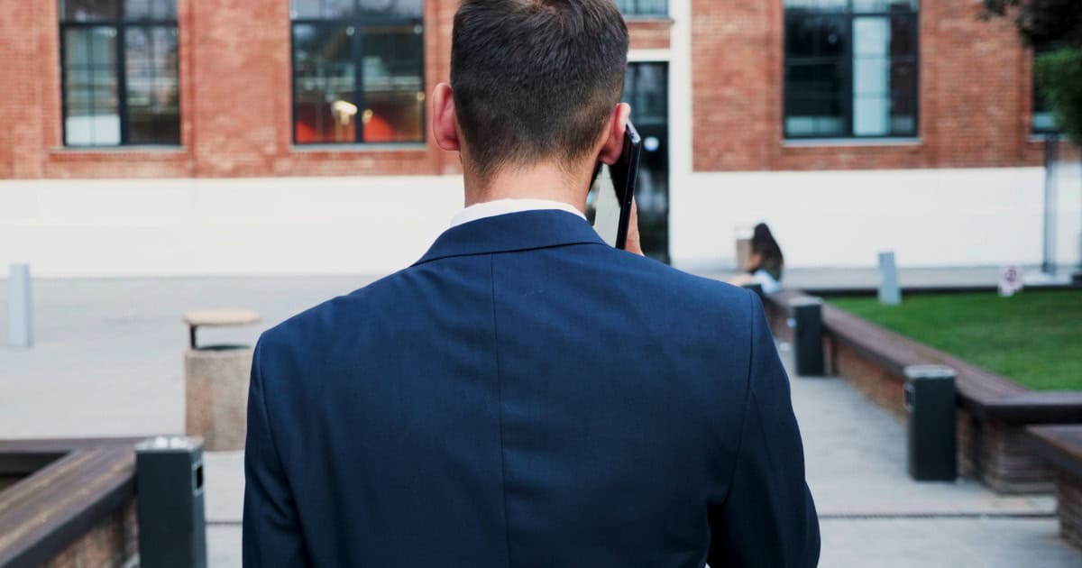 Security guard in suit talking on mobile phone outside a modern building.